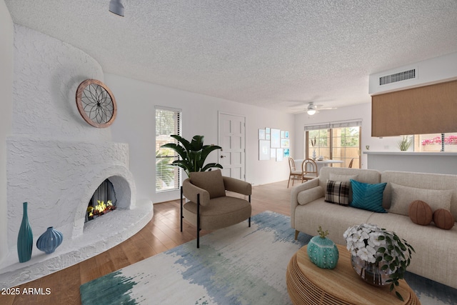 living area with a premium fireplace, visible vents, a textured ceiling, and wood finished floors