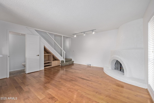 unfurnished living room with wood-type flooring, rail lighting, a large fireplace, and a textured ceiling