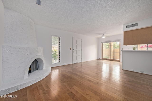 unfurnished living room with hardwood / wood-style flooring, ceiling fan, a textured ceiling, and a fireplace