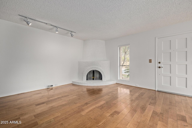 unfurnished living room with a brick fireplace, hardwood / wood-style floors, a textured ceiling, and rail lighting