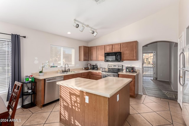 kitchen with appliances with stainless steel finishes, sink, light tile patterned floors, a center island, and lofted ceiling