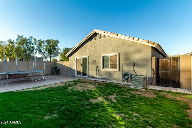 rear view of property featuring central AC unit, a trampoline, a patio, and a yard