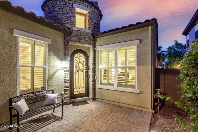 4519 N 29th Way, Phoenix, AZ 85016 - exterior entry at dusk with stucco siding, a patio, a tiled roof, and stone siding