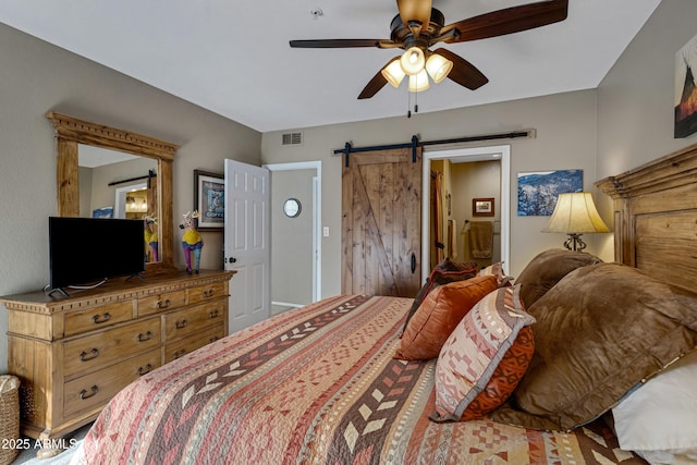 bedroom featuring ensuite bathroom, a barn door, and ceiling fan