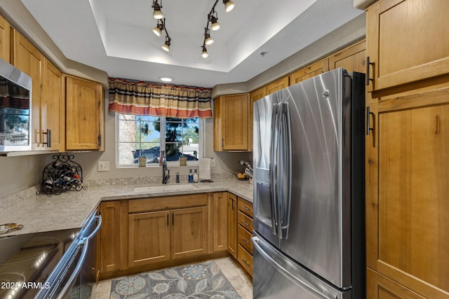 kitchen with sink, a tray ceiling, light stone countertops, and appliances with stainless steel finishes