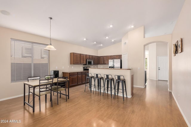 kitchen with arched walkways, light countertops, stainless steel microwave, light wood-style floors, and freestanding refrigerator