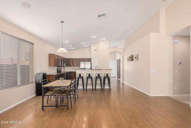 dining space featuring arched walkways, lofted ceiling, visible vents, light wood-type flooring, and baseboards