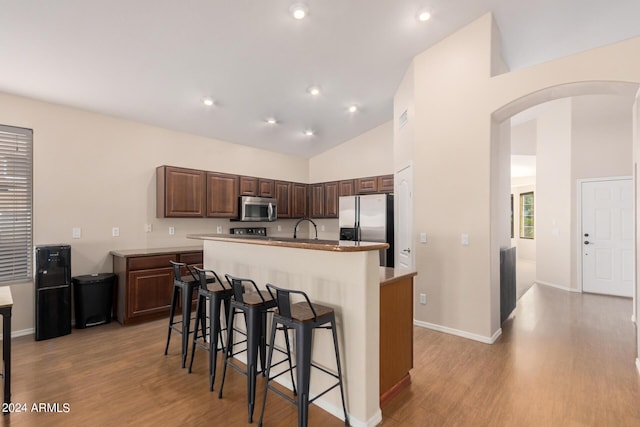 kitchen featuring arched walkways, appliances with stainless steel finishes, light wood finished floors, and an island with sink