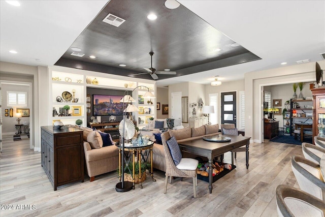 living room with a raised ceiling, ceiling fan, and light hardwood / wood-style flooring