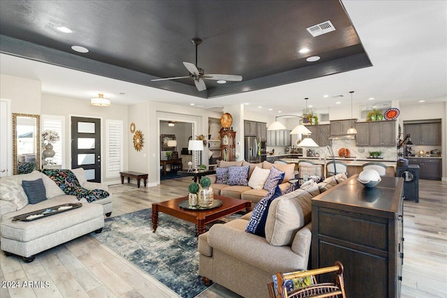 living room featuring a raised ceiling, light hardwood / wood-style floors, and ceiling fan