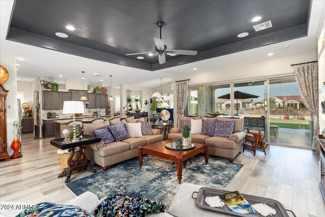 living room featuring ceiling fan, a raised ceiling, and light hardwood / wood-style flooring