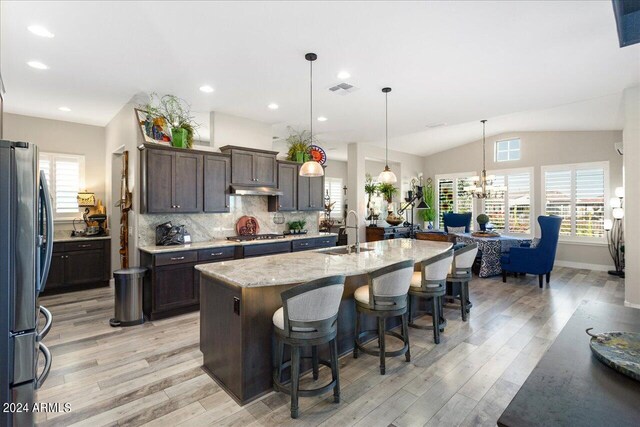 kitchen featuring vaulted ceiling, pendant lighting, stainless steel appliances, a center island with sink, and sink