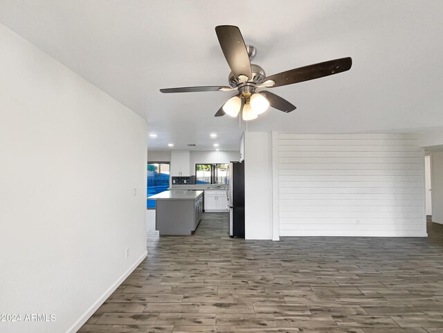 unfurnished living room with ceiling fan, wood walls, and dark hardwood / wood-style flooring