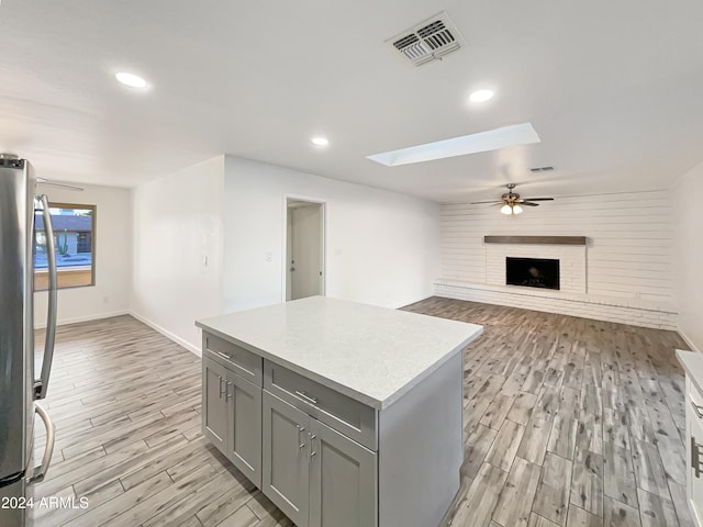 kitchen with a center island, a skylight, ceiling fan, a fireplace, and light hardwood / wood-style floors