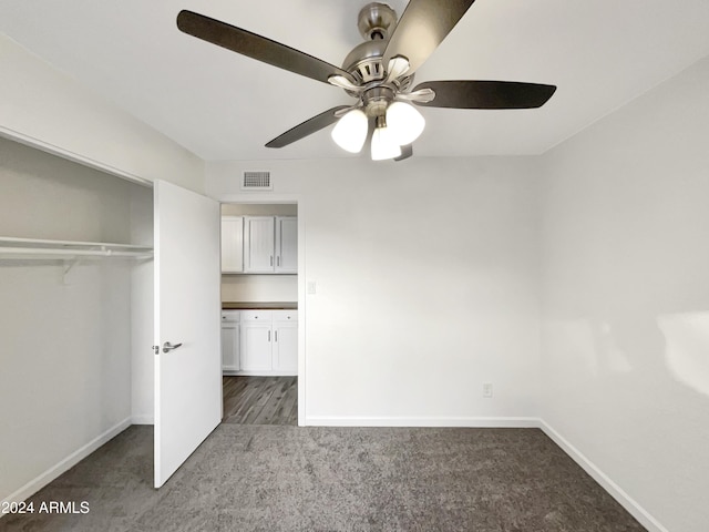 unfurnished bedroom with dark colored carpet, ceiling fan, and a closet