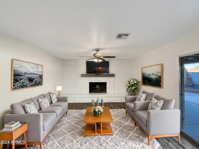 living room featuring hardwood / wood-style flooring, ceiling fan, wood walls, and a brick fireplace