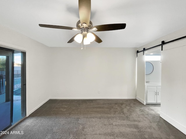 spare room featuring a barn door, dark carpet, and ceiling fan