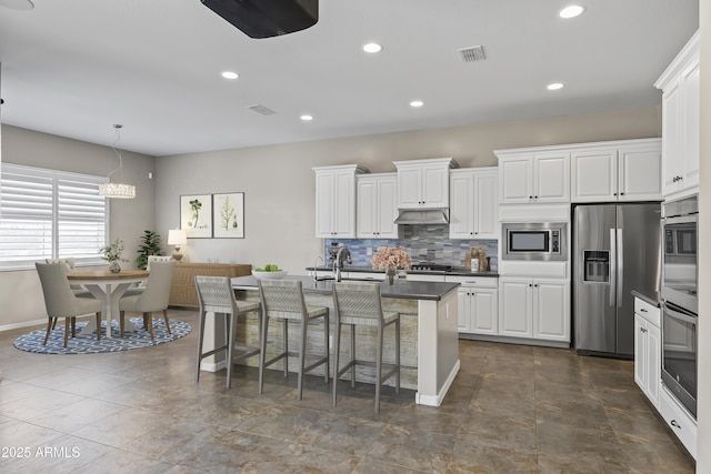 kitchen with visible vents, under cabinet range hood, dark countertops, stainless steel appliances, and a breakfast bar area