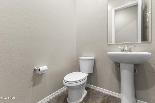 bathroom with a textured wall, toilet, and baseboards