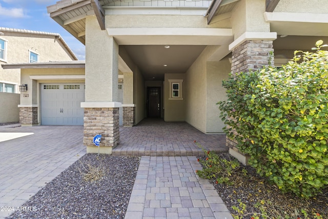 doorway to property featuring driveway, stucco siding, stone siding, and an attached garage