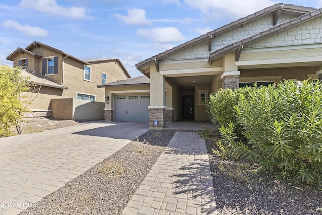 craftsman inspired home featuring an attached garage, stucco siding, stone siding, and decorative driveway