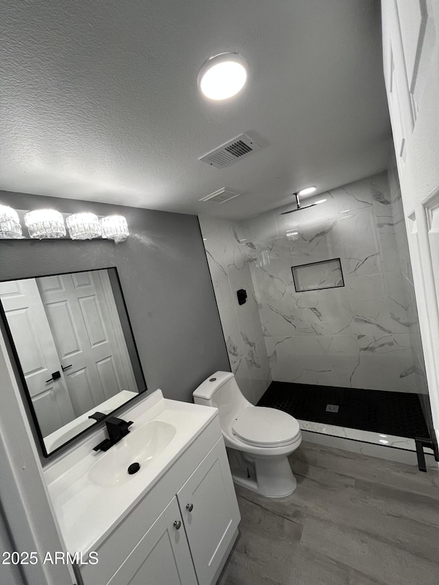 bathroom featuring hardwood / wood-style floors, vanity, a tile shower, a textured ceiling, and toilet