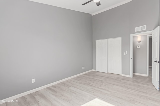 unfurnished bedroom with a towering ceiling, light hardwood / wood-style floors, a closet, and ceiling fan