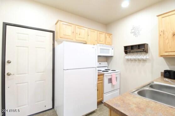 kitchen with light tile patterned floors, sink, light brown cabinetry, and white appliances