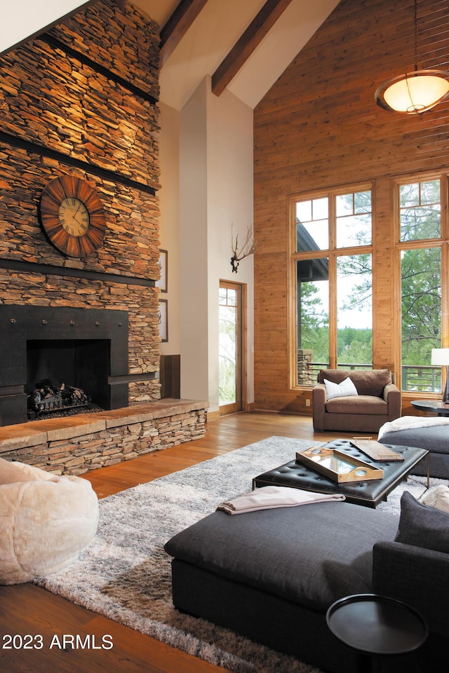 living room featuring hardwood / wood-style flooring, wooden walls, high vaulted ceiling, and a stone fireplace