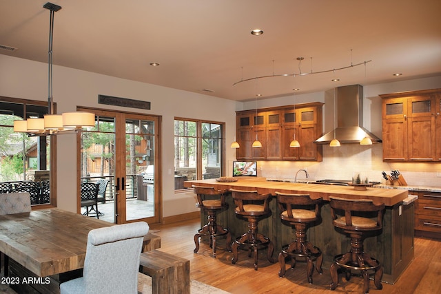 bar with butcher block counters, hanging light fixtures, tasteful backsplash, wall chimney exhaust hood, and light wood-type flooring