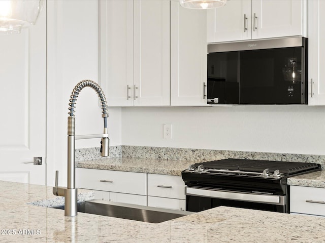 4041 S 176th Dr, Goodyear, AZ 85338 - kitchen with stainless steel microwave, black range with gas cooktop, white cabinetry, light stone counters, and hanging light fixtures