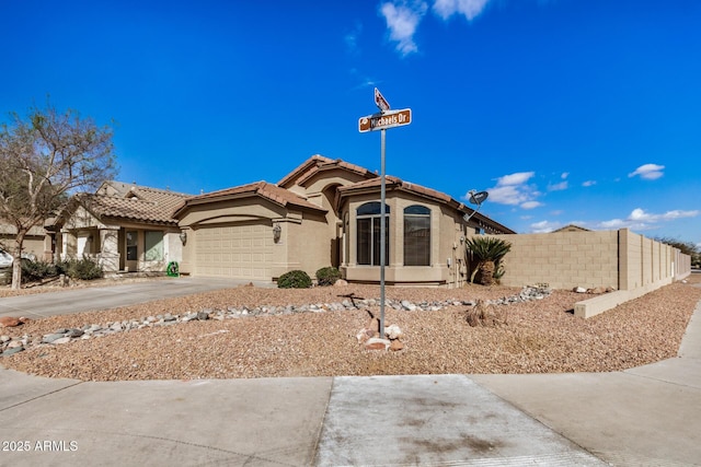 view of front facade with a garage, concrete driveway, a tiled roof, fence, and stucco siding