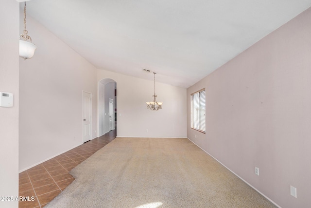 carpeted empty room with arched walkways, tile patterned flooring, and an inviting chandelier