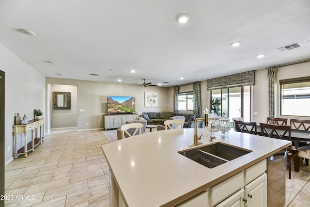 kitchen featuring a sink, visible vents, open floor plan, light countertops, and an island with sink