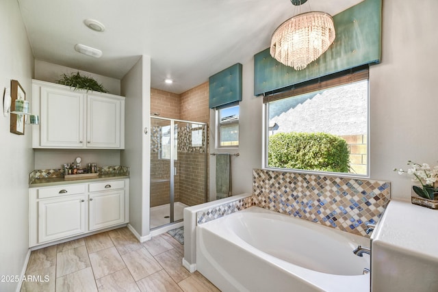 bathroom featuring vanity, baseboards, a shower stall, a bath, and an inviting chandelier