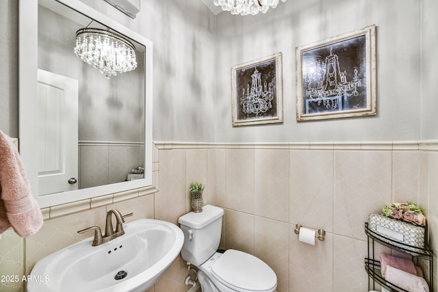 half bath with toilet, a wainscoted wall, a chandelier, and a sink