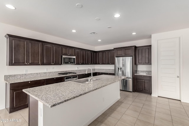 kitchen featuring an island with sink, appliances with stainless steel finishes, light stone countertops, a sink, and recessed lighting