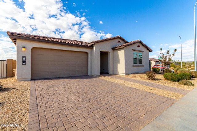 mediterranean / spanish house featuring decorative driveway, a tiled roof, an attached garage, and stucco siding