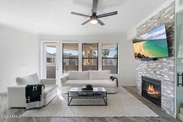 living room featuring a stone fireplace, ceiling fan, crown molding, and hardwood / wood-style flooring