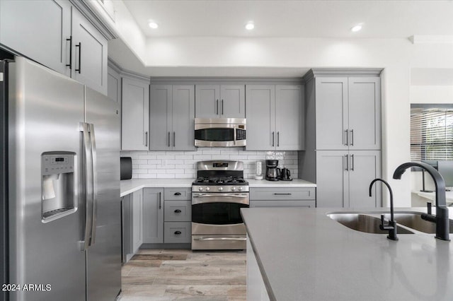 kitchen featuring light wood-type flooring, gray cabinets, appliances with stainless steel finishes, sink, and tasteful backsplash