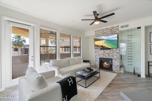 living room featuring a stone fireplace, a healthy amount of sunlight, wood-type flooring, and ceiling fan