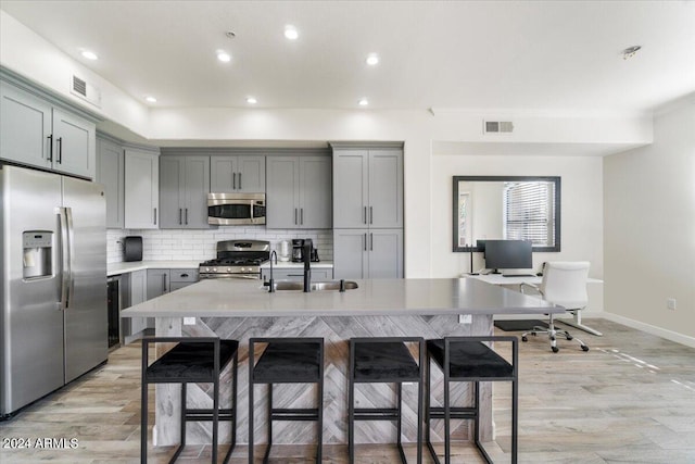 kitchen featuring stainless steel appliances, light hardwood / wood-style floors, a center island with sink, tasteful backsplash, and a kitchen breakfast bar