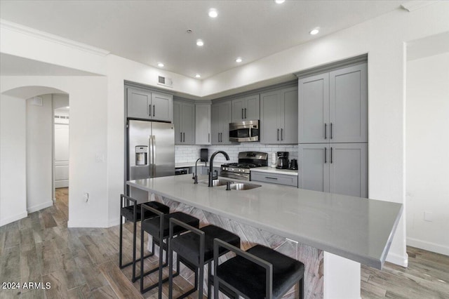 kitchen with wood-type flooring, appliances with stainless steel finishes, backsplash, and a kitchen island with sink