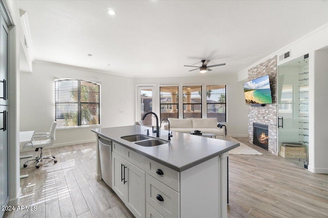 kitchen featuring brick wall, a kitchen island with sink, a fireplace, sink, and light wood-type flooring