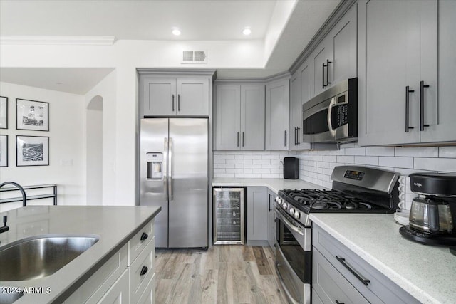 kitchen with appliances with stainless steel finishes, tasteful backsplash, wine cooler, and light wood-type flooring