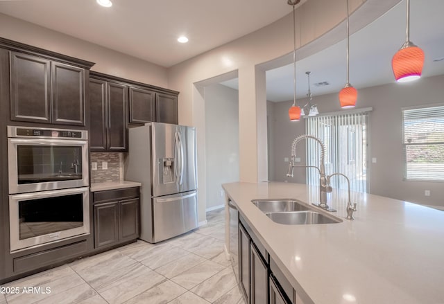 kitchen featuring decorative light fixtures, stainless steel appliances, dark brown cabinets, light countertops, and a sink