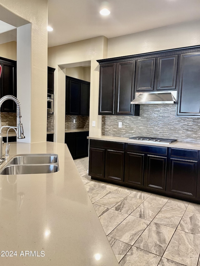 kitchen with under cabinet range hood, stainless steel gas cooktop, light countertops, and a sink