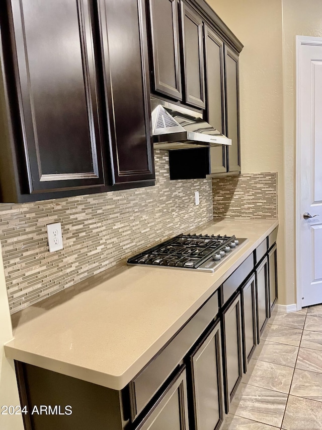 kitchen featuring tasteful backsplash, light countertops, dark brown cabinets, under cabinet range hood, and stainless steel gas stovetop