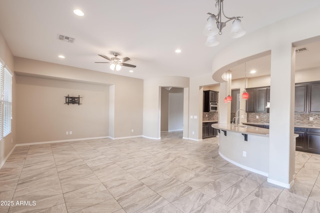 kitchen featuring tasteful backsplash, visible vents, a breakfast bar, decorative light fixtures, and light countertops