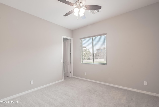 spare room with a ceiling fan, light colored carpet, visible vents, and baseboards